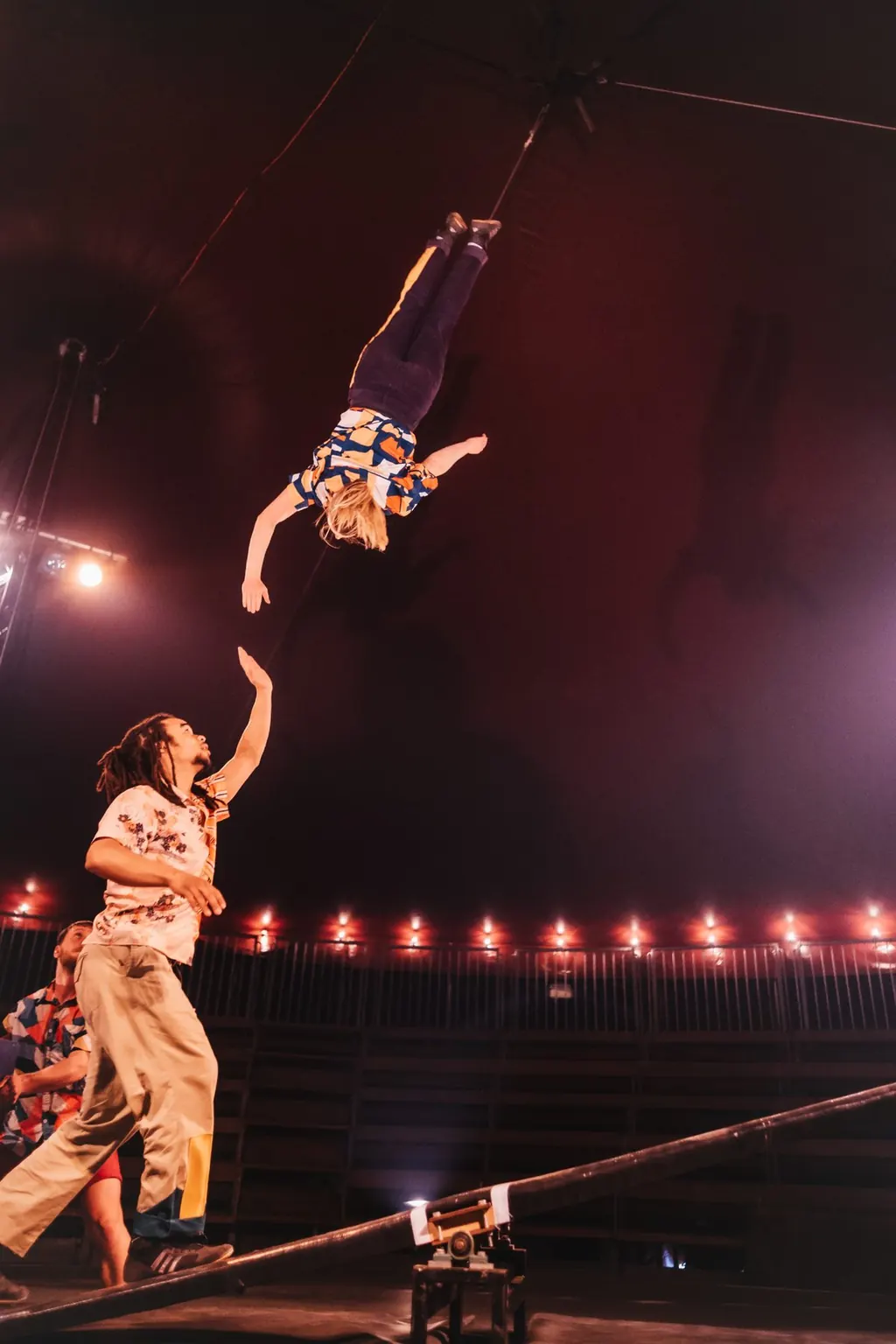 A teeterboard flyer somersaults above the ring inside the big top